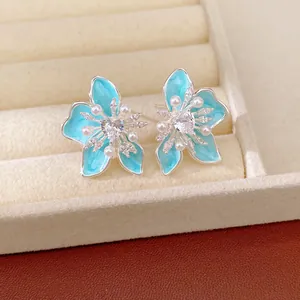 Macro view of light blue enamel flower earrings with sparkling heart zircons and pearls.