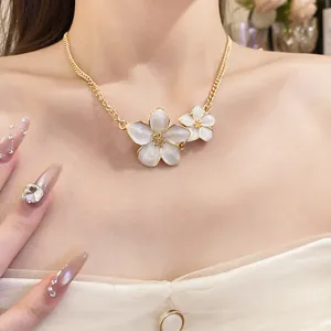 Detailed view of elegant gold-toned necklace with two white enamel flower pendants