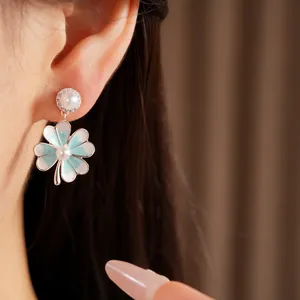 Detailed close-up of blue four-leaf clover stud earrings with pearls and zircon on ear