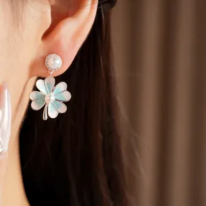 Close-up of blue clover earrings with pearls and zircons on model's ear