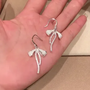 Detailed view of silver bow-knot earrings with shimmering zirconia tassels on a palm