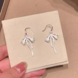 Detail view of elegant silver bow-knot earrings featuring long zircon tassels on a pad.