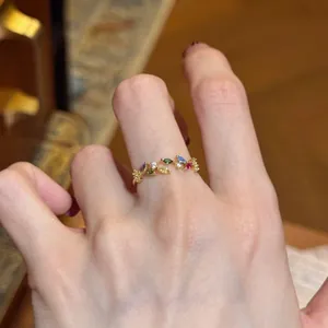 Detailed view of a gold-tone leaf open ring with colorful zircon stones on a hand.