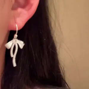 Detailed close-up view of elegant silver bow tassel earrings with zircon stones on ear.