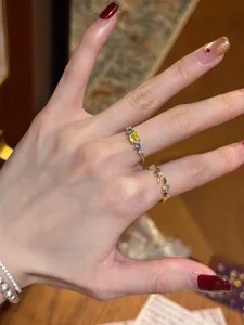 Detailed view of two delicate gold leaf-shaped rings with colorful zirconia worn on a hand.