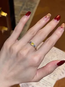 Detailed view of an elegant gold ring set with yellow and blue gemstones on a model's hand