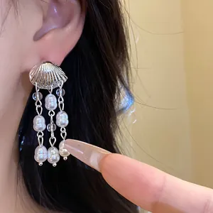 Close-up detail of elegant silver shell and pearl tassel drop earrings worn on ear
