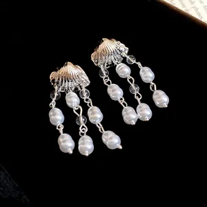 Detailed view of silver shell stud earrings with white pearl tassels on black background