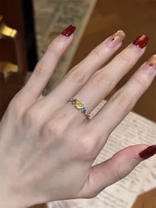 Dainty gold-plated ring featuring yellow and blue zircon stones on a manicured hand