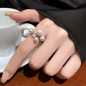 Close-up of elegant adjustable open ring with shimmering pearls and zircon on finger.