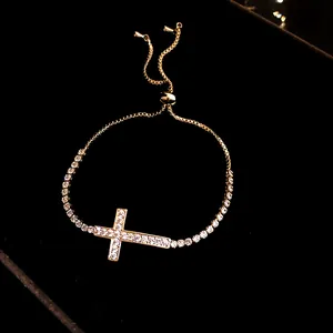Dettaglio di un bracciale con croce dorata e zirconi scintillanti su velluto nero.