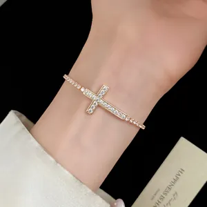 Primo piano di un elegante bracciale a croce placcato oro con zirconi al polso.