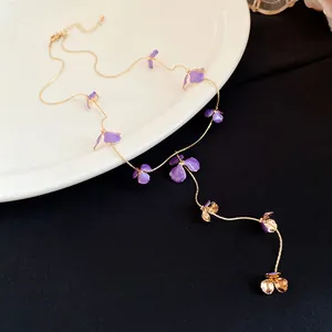 Close-up of golden necklace with purple enamel flower pendants on a white plate
