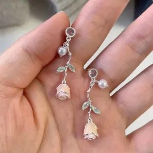 Close-up detail of silver dripping oil rose flower earrings with pearls and crystals.