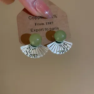 Dettaglio di orecchini d'argento a ventaglio con perline verdi e motivi di bambù.