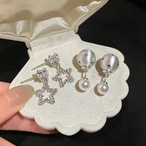 Close-up detail of silver needle star stud and pearl ball drop earrings in shell box