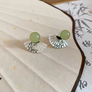 Dettaglio degli orecchini a ventaglio con motivi a inchiostro di bambù e perline di giada verde.