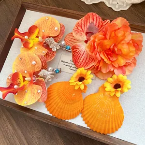 Detail of tropical fabric flower hair clips with shells and pearls in vibrant orange tones.
