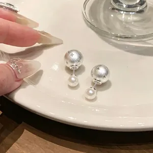 Close-up of silver star-engraved sphere earrings with elegant pearls on a white plate.