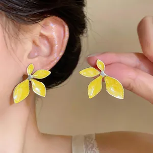 Close-up detail of bright yellow enamel flower stud earrings worn on a model's ear