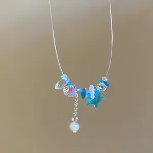 Detailansicht einer zierlichen Halskette mit blauem Seestern, Muschelanhängern und Perle.