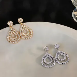Elegant gold and silver teardrop zircon hollow stud earrings on white ceramic plate