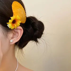 Close-up of a vacation-style yellow seashell and sunflower hair clip on a model.