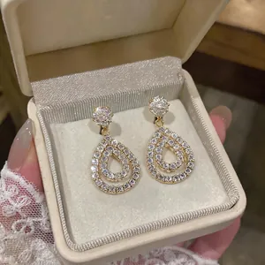 Elegant vintage-style gold water drop hollow earrings with brilliant zircon in a cream jewelry box.