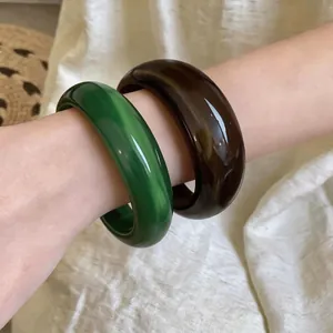 Élégants joncs géométriques en acrylique marbré vert et marron portés au poignet