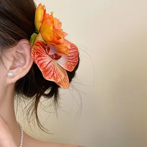 Close-up detail of a vibrant orange fabric orchid flower hair clip worn on a side bun.