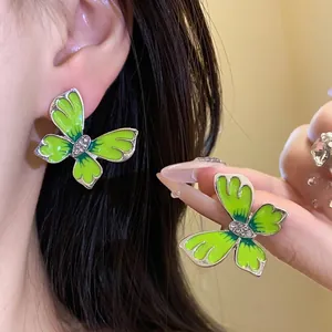 Elegant green butterfly earrings with sparkly rhinestone center on a female model's ear
