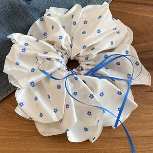 Gros plan d'un grand chouchou blanc en tissu avec motifs floraux bleus et un nœud.