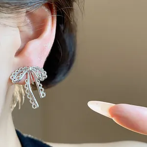 Detailed macro view showing a delicate silver lace bow clip-on earring worn on a model's ear