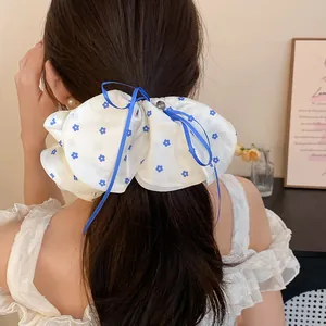 Détail d'un grand chouchou blanc à motifs floraux bleus avec un nœud sur les cheveux