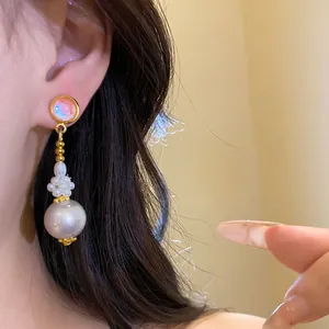 Dettaglio di un elegante orecchino a pendente con resina rosa e perla bianca.