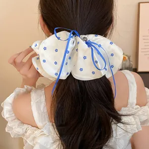 Vue arrière détaillée d'un chouchou en tissu à fleurs blanches et ruban bleu sur cheveux.