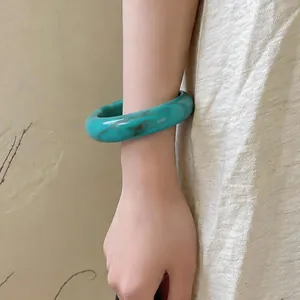 Gros plan d'un élégant bracelet jonc en acrylique marbré sarcelle porté au poignet.