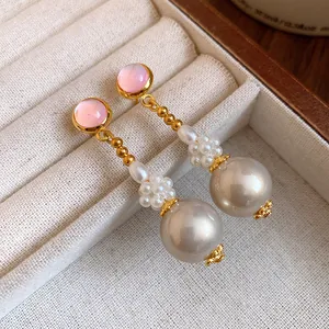 Dettaglio macro di eleganti orecchini pendenti in resina rosa e perle grigie in scatola.