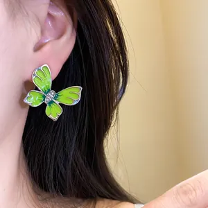 Close-up of green enamel butterfly earring with small rhinestones on model's ear.