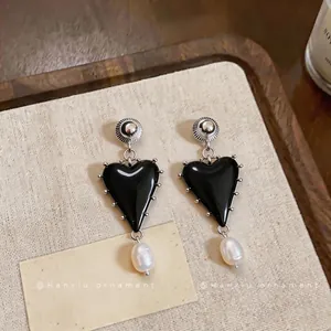 Vintage black resin heart earrings with pearl drops on textured beige background