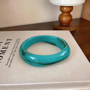 Gros plan d'un bracelet en acrylique marbré turquoise au design géométrique irrégulier.