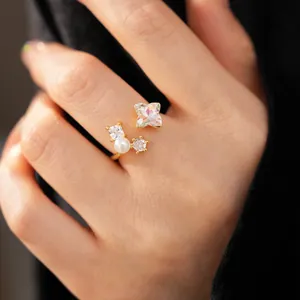 Close-up detail of a gold open ring featuring an iridescent flower stone and a small pearl accent