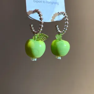 Nahaufnahme von grünen Harz-Apfel-Ohrringen mit eleganten silbernen Perlenreifen.