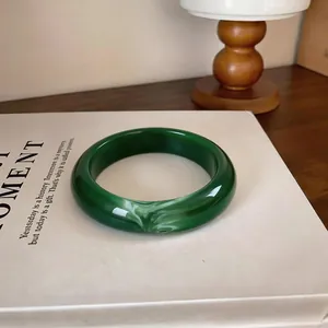 Détail d'un bracelet jonc en acrylique vert foncé avec marbrure blanche sur un livre blanc
