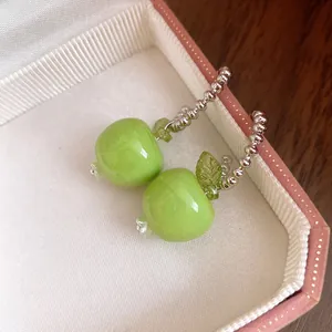 Detailansicht von süßen grünen Harz-Apfel-Ohrhängern mit eleganten silbernen Perlenreifen.