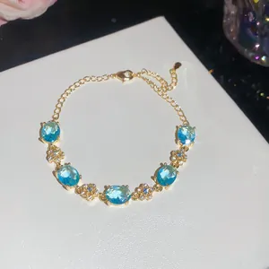 Close-up of 18k gold plated bracelet with oval blue zircons and flower details