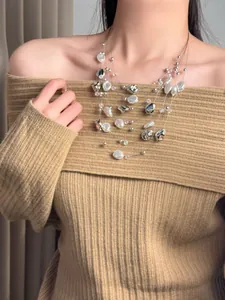 Detail view of an elegant multi-layered pearl and silver bead necklace worn on a beige sweater