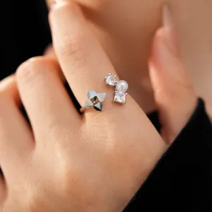 Close-up of an elegant open ring featuring a faceted flower and pearl detail on a finger.