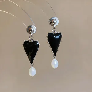 Elegant close-up of vintage black heart resin earrings featuring a white pearl drop