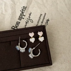 Close-up of sweet gradient heart studs and silver floral hoop earrings on a velvet tray